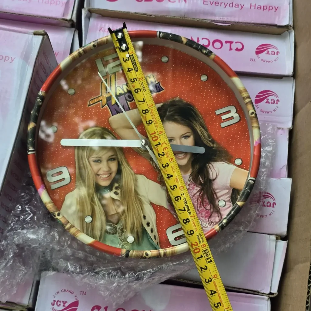 Reloj de pared Hannah Montana con imágenes de Miley Cyrus y cinta métrica sobre cajas de embalaje. by Remates Narvaja