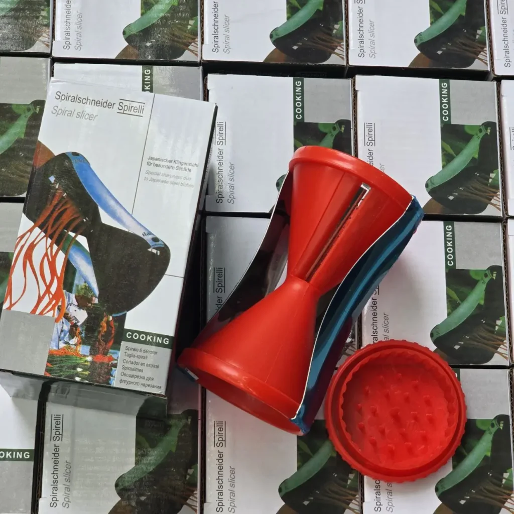 Rebanador espiral de verduras rojo Spirelli sobre cajas de producto apiladas. by Remates Narvaja