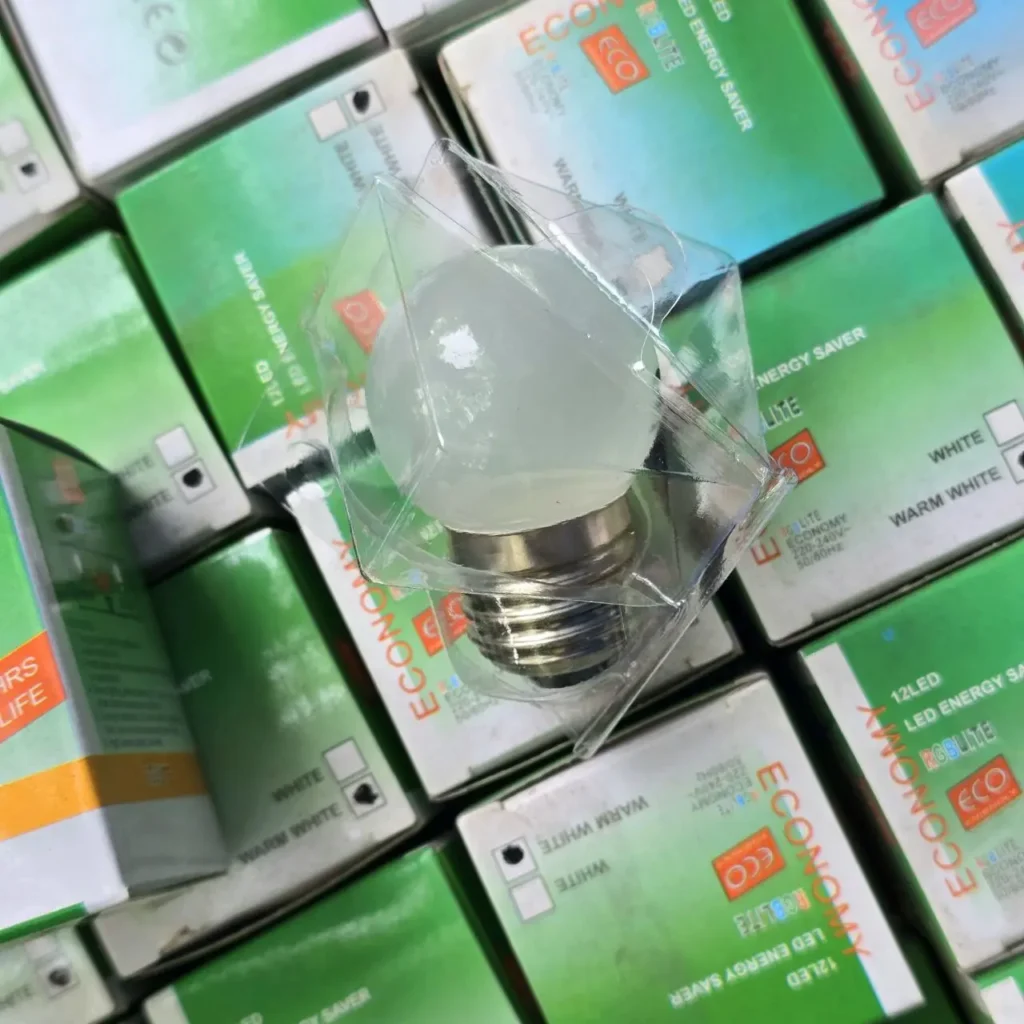 Bombilla LED esmerilada en su empaque, rodeada de cajas de luces LED de ahorro energético. by Remates Narvaja