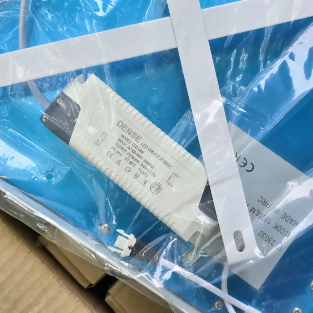 Controlador LED DENSE de 24W en su embalaje, junto a un panel de luz LED. by Remates Narvaja