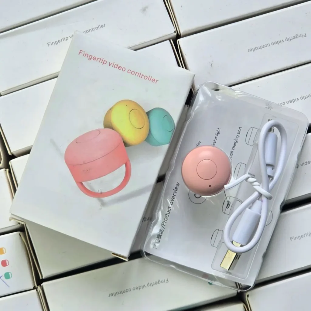 Controlador de video de dedo rosa con cable USB en su empaque, junto a la caja del producto que muestra versiones en rosa, amarillo y azul. by Remates Narvaja