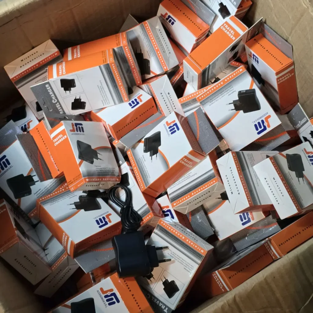 Caja llena de cargadores de viaje JTM en cajas blancas y naranjas. by Remates Narvaja