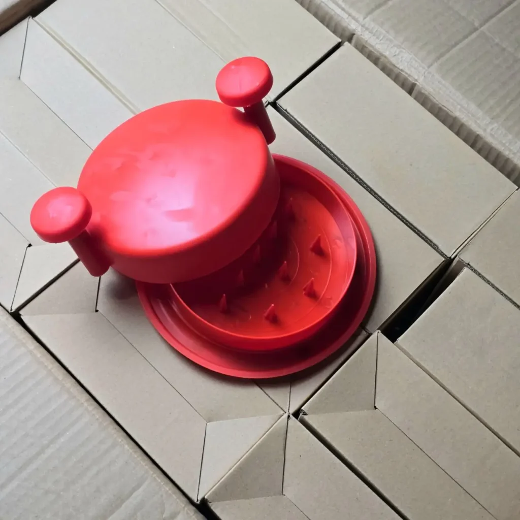 Picador de alimentos manual rojo con púas, sobre cajas de cartón. by Remates Narvaja