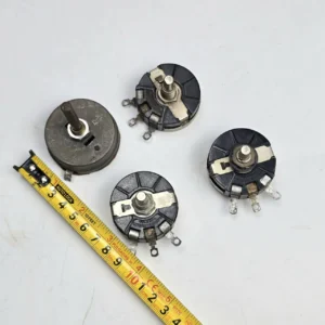 Cuatro potenciómetros vintage de diferentes tamaños y una cinta métrica amarilla sobre una superficie blanca. by Remates Narvaja
