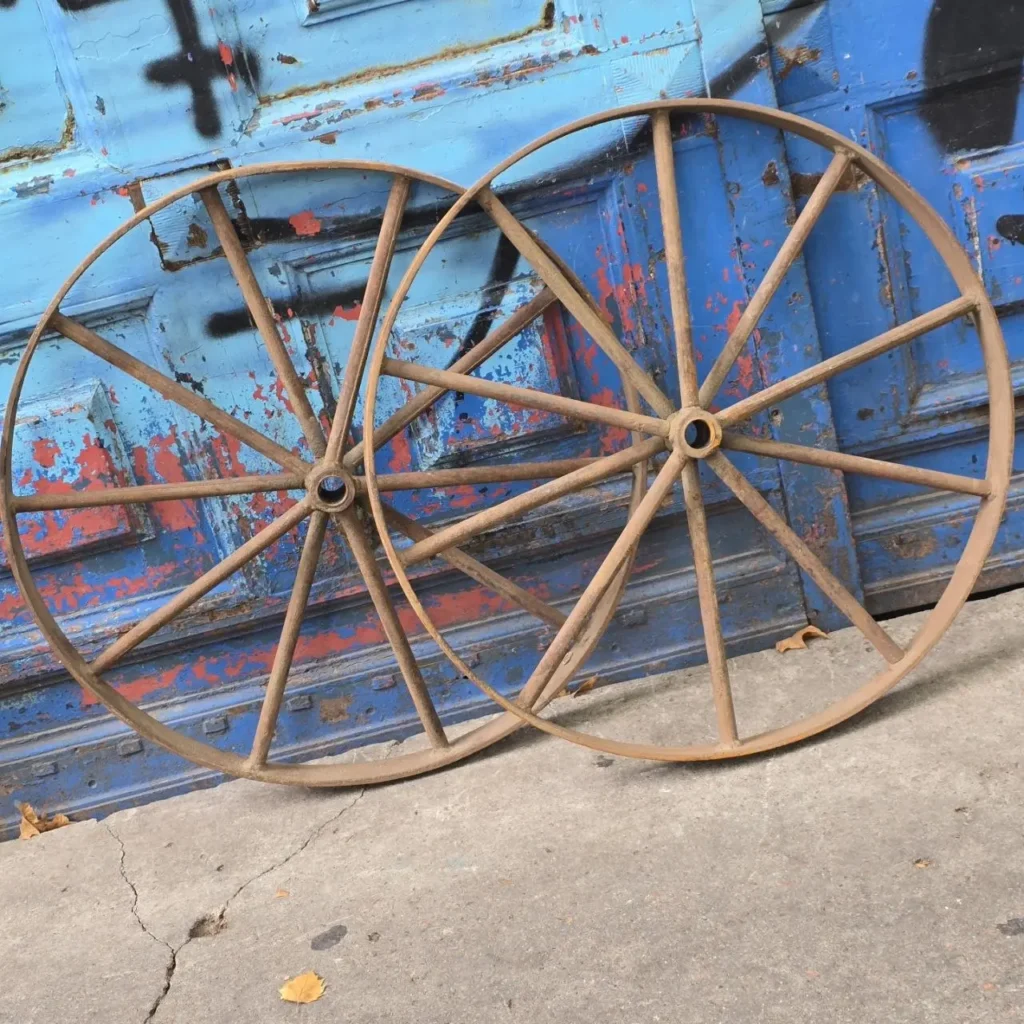 Dos ruedas metálicas oxidadas apoyadas contra una pared azul con pintura descascarada. by Remates Narvaja