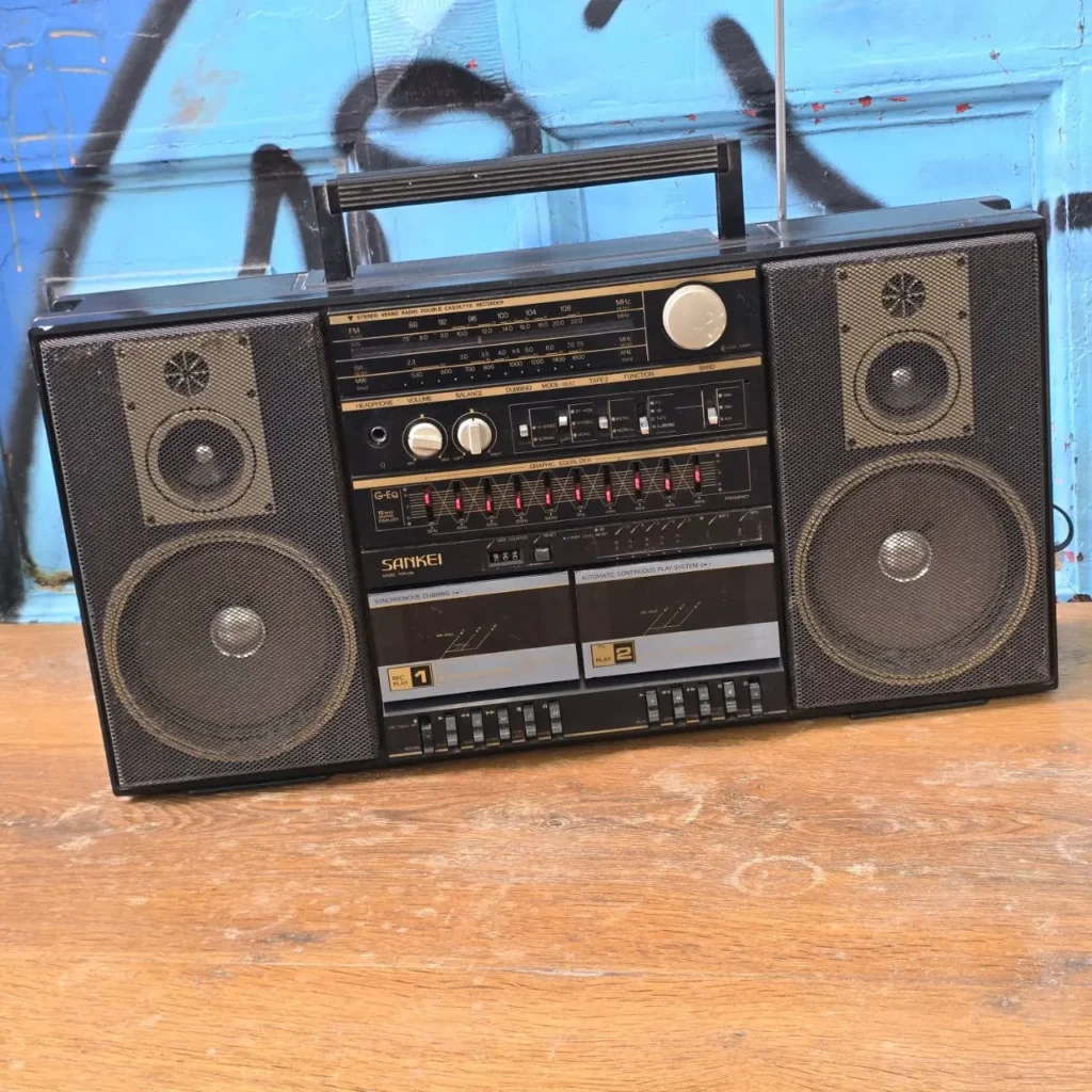 Sankei retro boombox con doble reproductor de casetes, radio y ecualizador gráfico sobre superficie de madera, frente a una pared azul con by Remates Narvaja