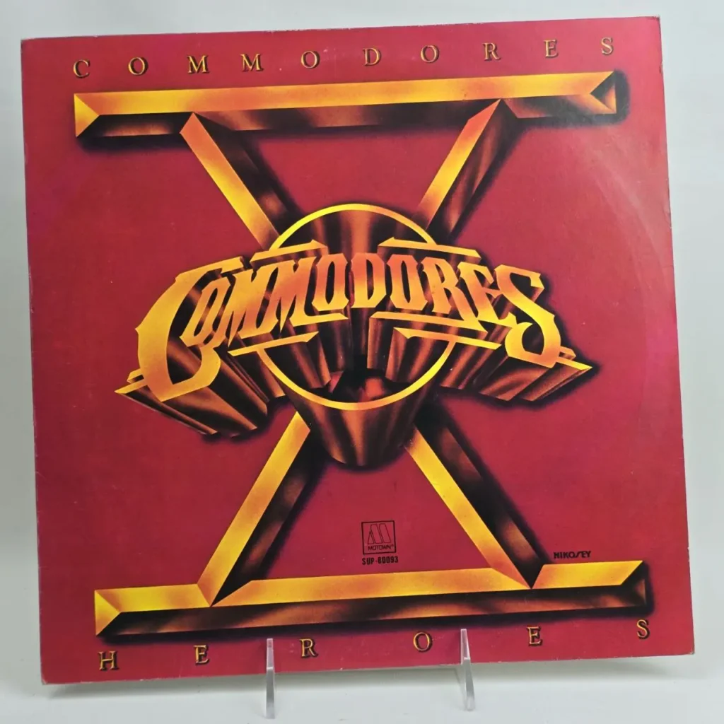 Portada del álbum de vinilo The Commodores Heroes, roja con una X dorada y el logo 3D. by Remates Narvaja