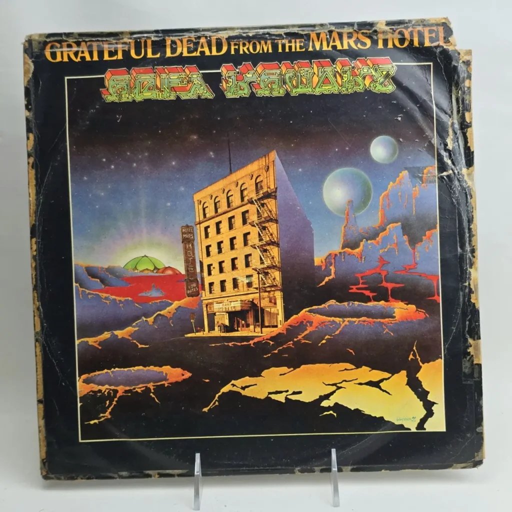 Portada del álbum de vinilo Grateful Dead From the Mars Hotel, mostrando un hotel en un paisaje marciano con lava y planetas. by Remates Narvaja