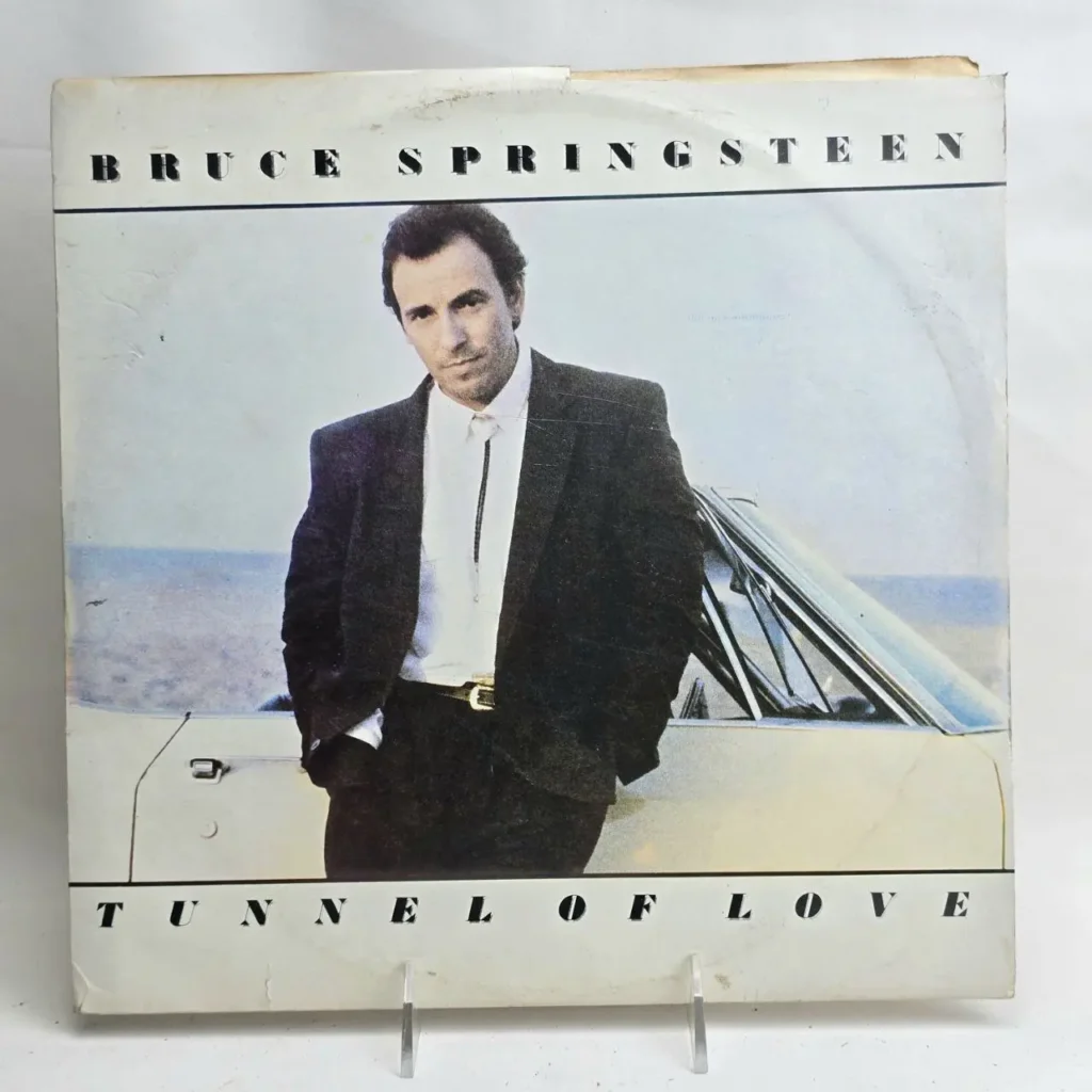 Portada del álbum Tunnel of Love de Bruce Springsteen, con él en traje junto a un coche. by Remates Narvaja