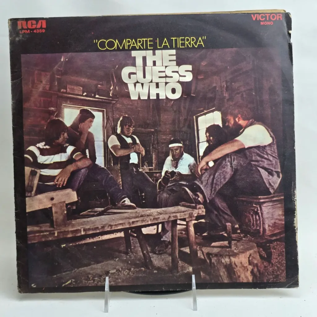 Portada del álbum de vinilo "Comparta La Tierra" de The Guess Who, con los miembros de la banda sentados en un ambiente rústico. by Remates Narvaja