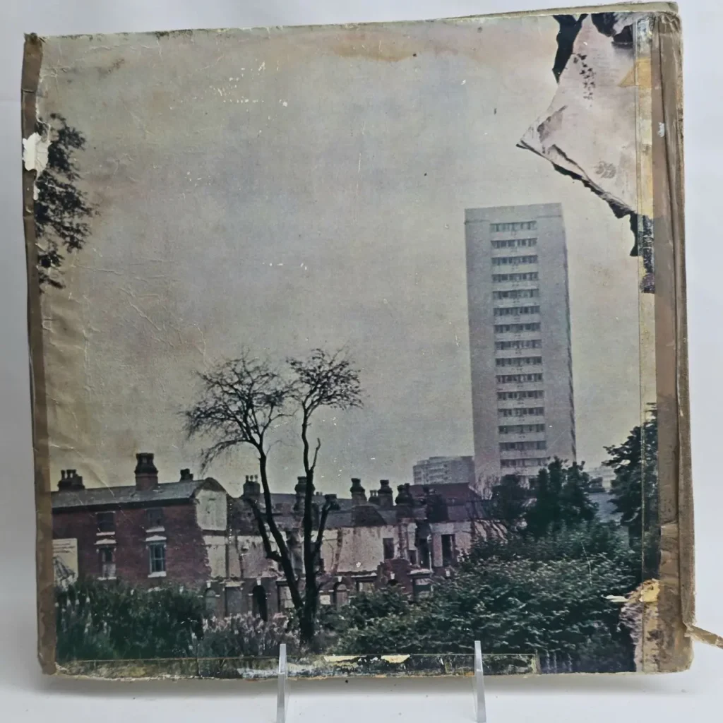 Cubierta de álbum o libro con un edificio de apartamentos alto, casas de ladrillo y árboles desnudos en un paisaje urbano desgastado. by Remates Narvaja