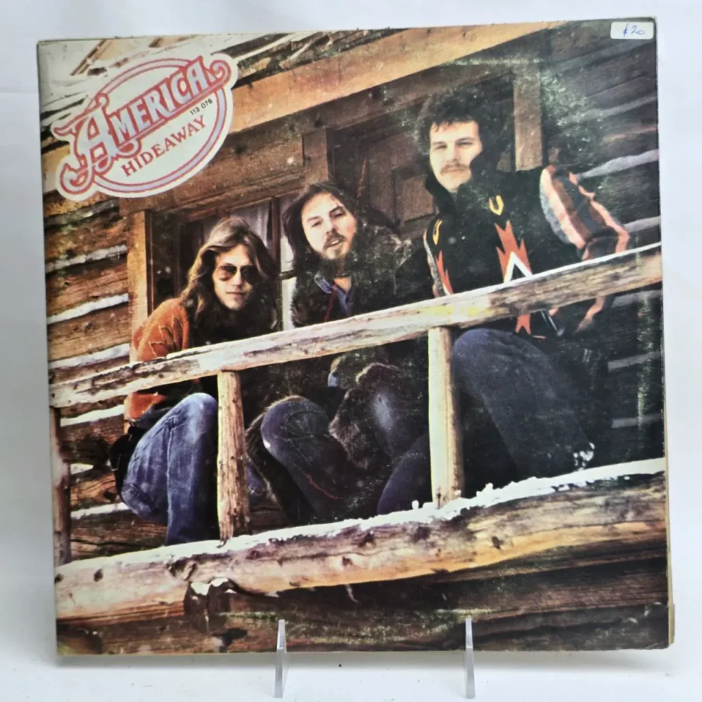 Portada del álbum America Hideaway con los tres miembros de la banda en una cabaña de madera. by Remates Narvaja