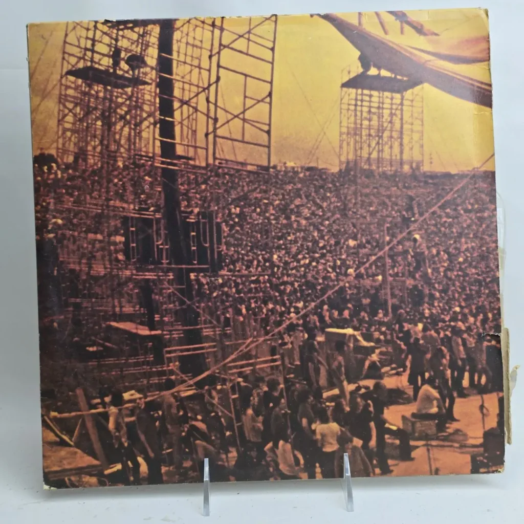 Festival de música al aire libre con gran multitud, andamios y un dirigible en el cielo. by Remates Narvaja