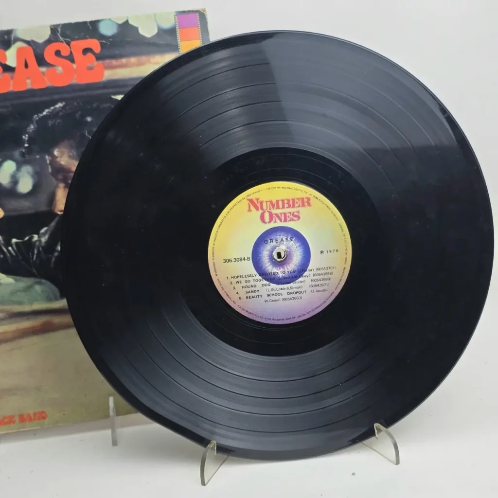 Disco de vinilo negro de la banda sonora de Grease con la etiqueta "NUMBER ONES" de 1978, mostrando canciones como "Hopelessly by Remates Narvaja