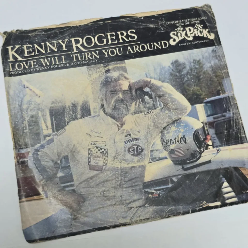 Portada del single de Kenny Rogers "Love Will Turn You Around" de la película Six Pack, con él en un traje de piloto de carreras. by Remates Narvaja