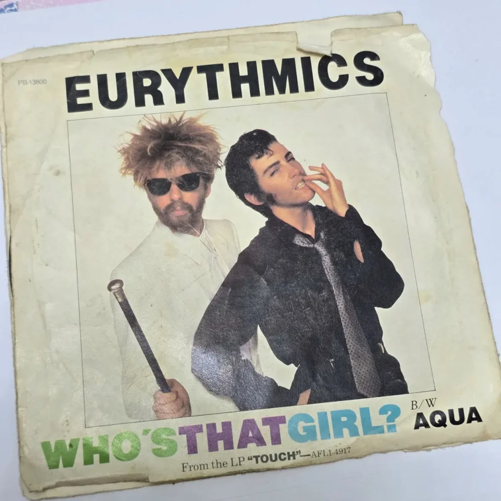 Portada del single "Who's That Girl?" de Eurythmics, mostrando a Dave Stewart con barba y gafas de sol, y a Annie Lennox mord by Remates Narvaja