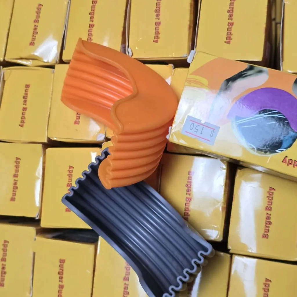 Soportes de silicona Burger Buddy para hamburguesas (naranja y gris) sobre cajas de producto. by Remates Narvaja