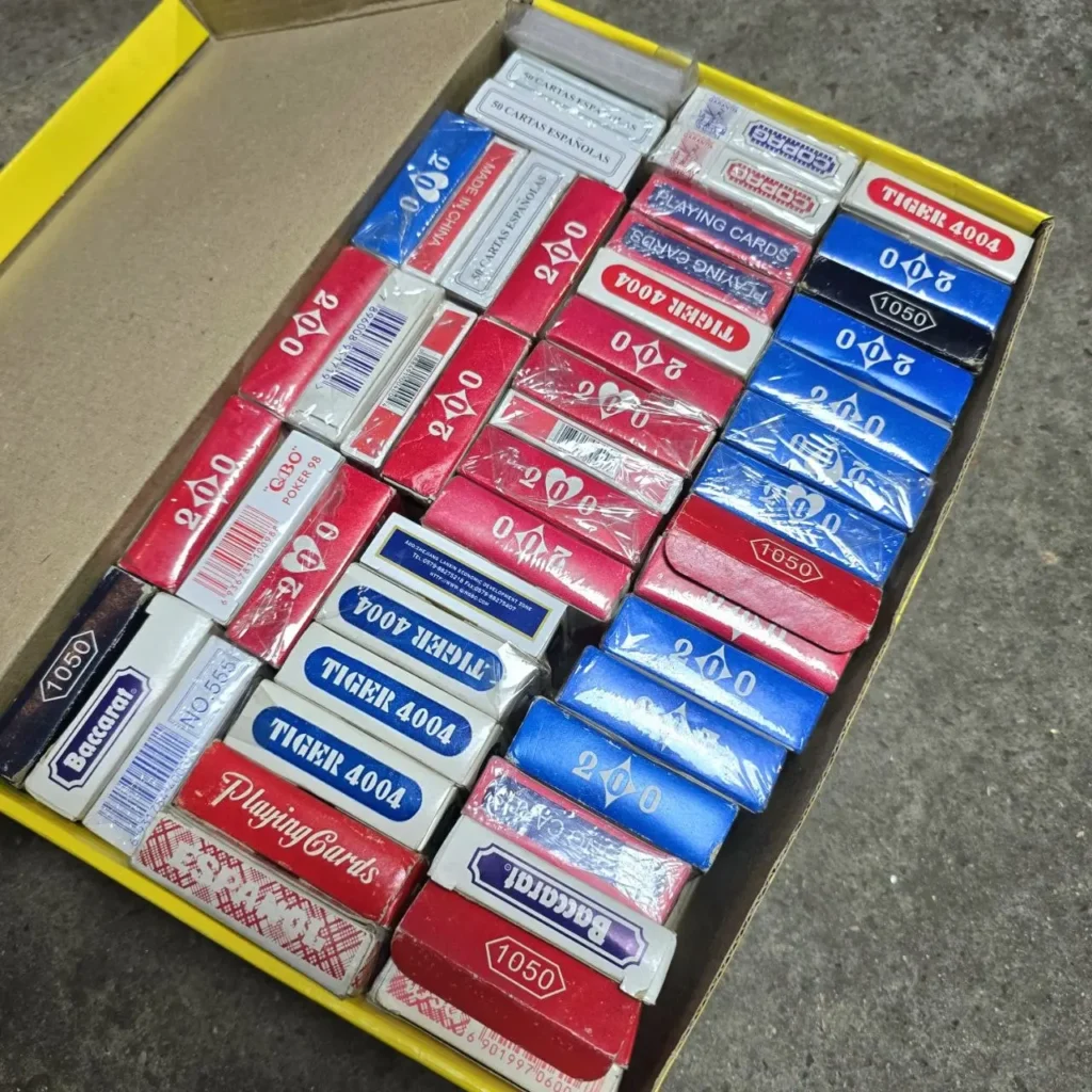 Caja de cartón llena de una variedad de mazos de naipes rojos, azules y blancos, incluyendo marcas como Tiger y Baccarat. by Remates Narvaja