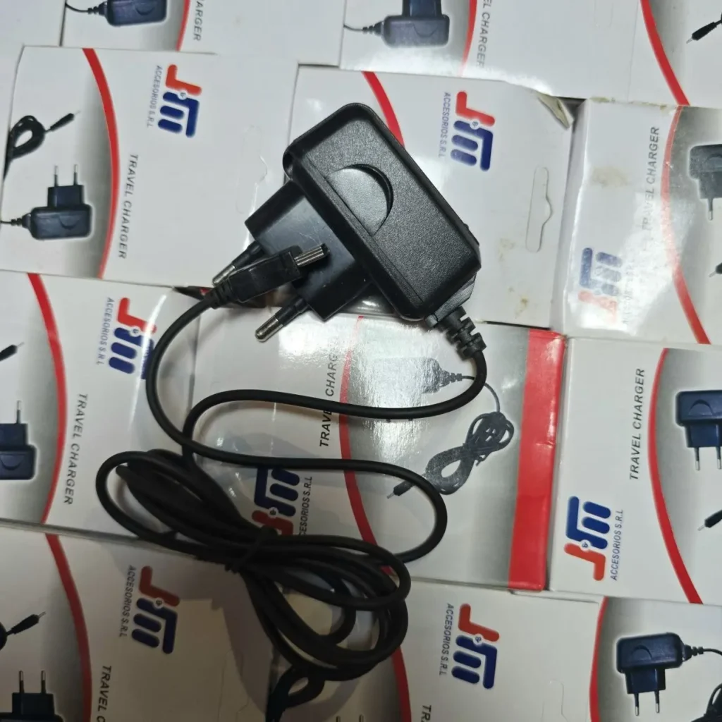 Cargador de viaje negro con adaptador de pared y cable sobre cajas de producto. by Remates Narvaja