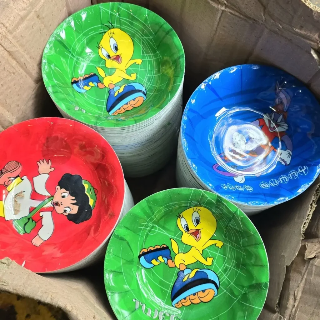 Pilas de platos de papel desechables de colores rojo, verde y azul con personajes de dibujos animados (Piolín, Bugs Bunny) en una caja. by Remates Narvaja