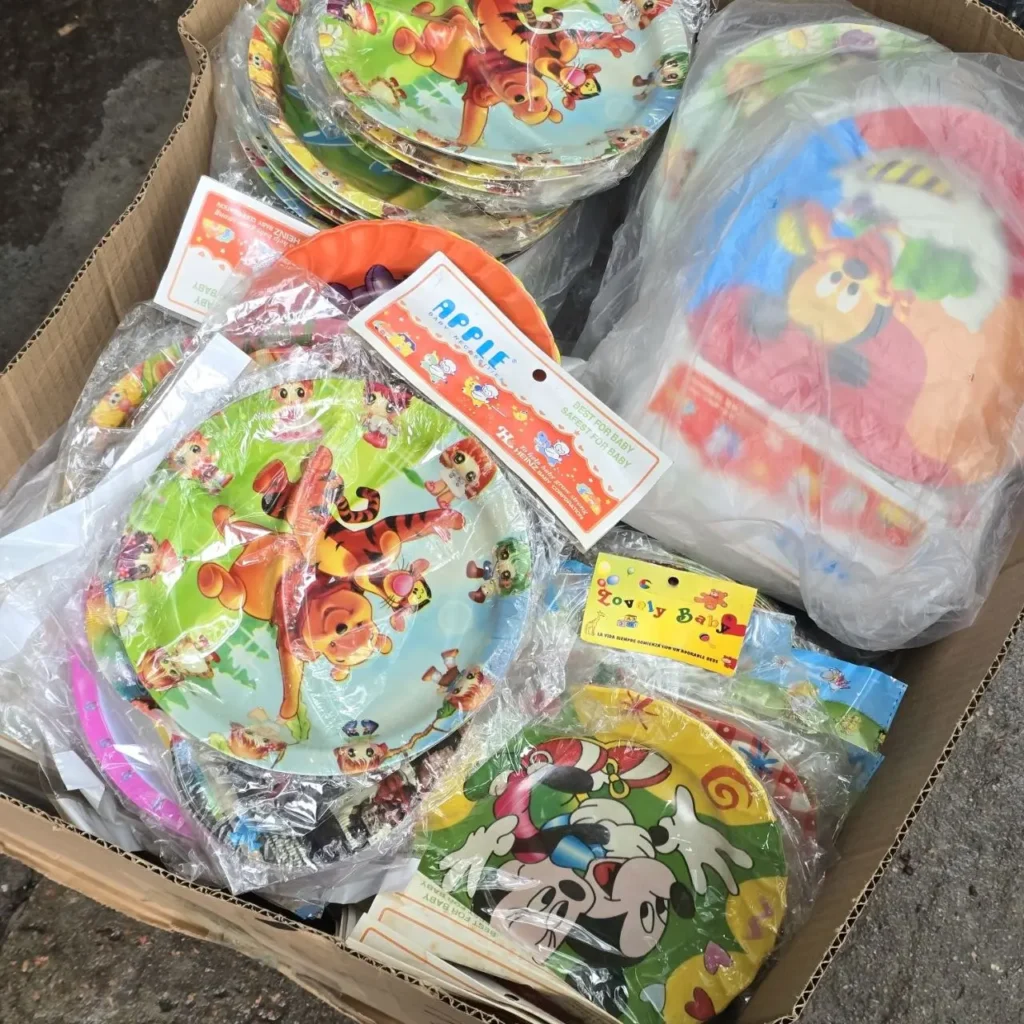 Caja llena de platos de fiesta infantiles envueltos en plástico, con personajes de dibujos animados como Winnie the Pooh y Mickey Mouse. by Remates Narvaja