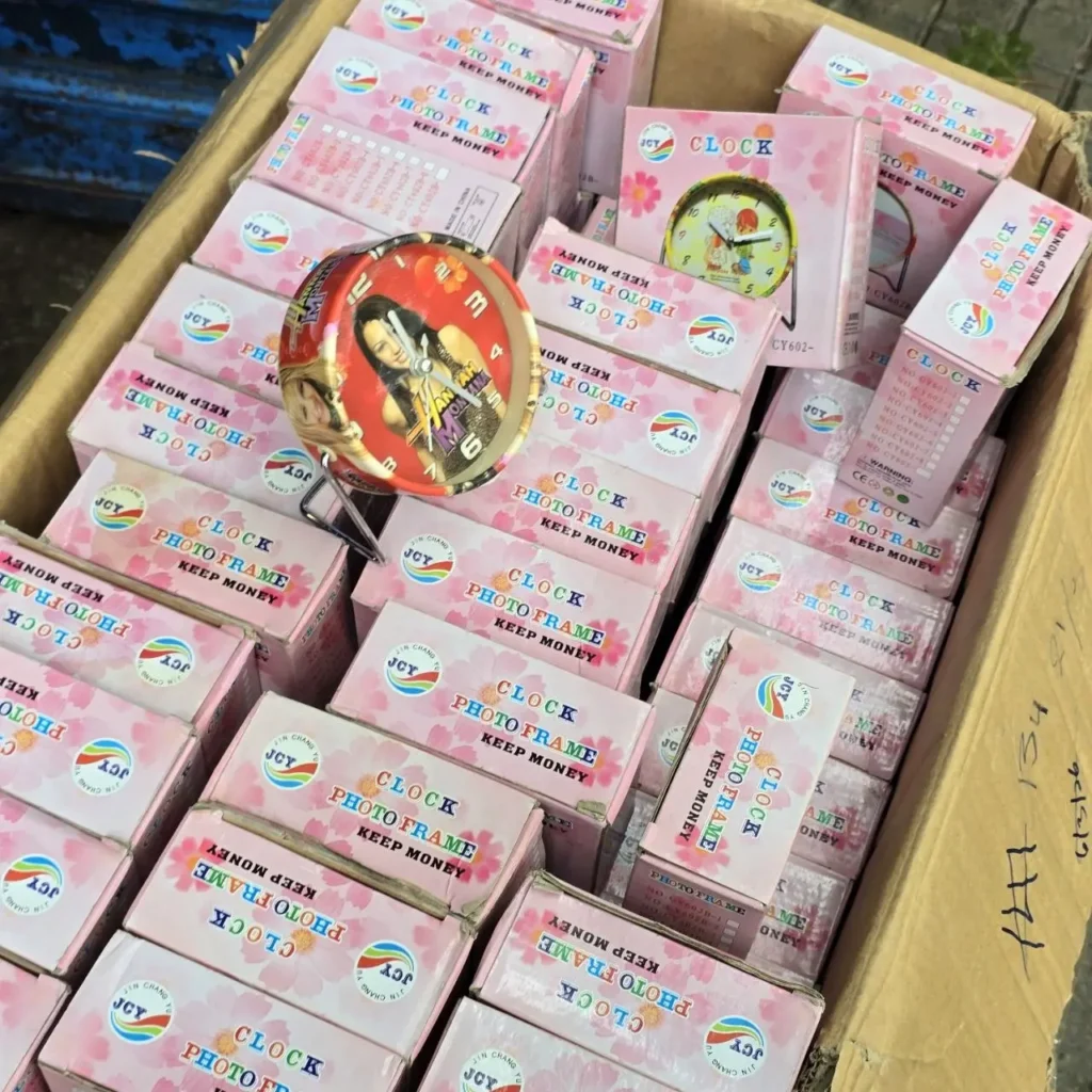 Caja de relojes y marcos de fotos JCY en cajas rosas, con un reloj de mesa mostrando una imagen de mujer. by Remates Narvaja