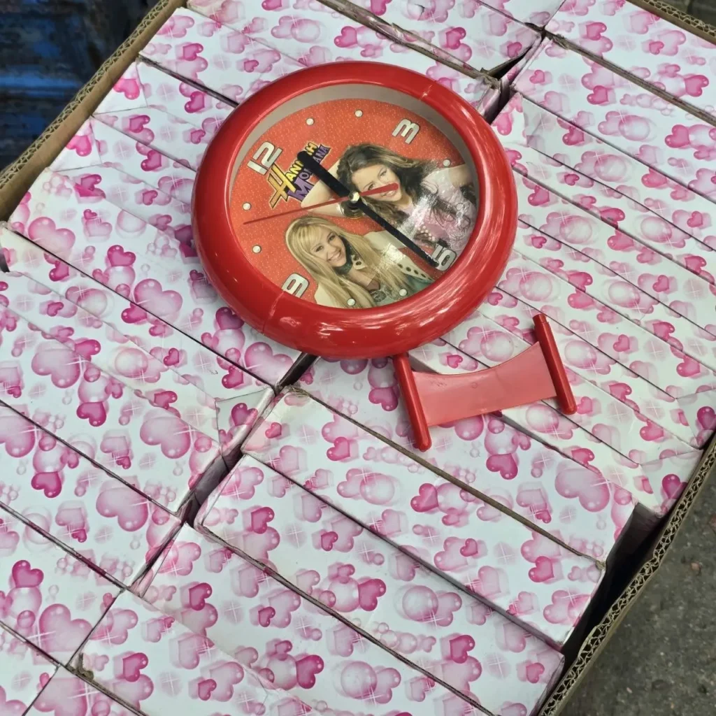 Reloj rojo de Hannah Montana con Miley Cyrus sobre cajas con patrón de corazones rosas. by Remates Narvaja