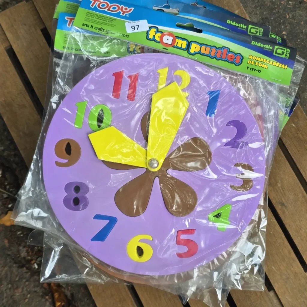 Reloj didáctico de fomi púrpura con números y manecillas de colores, en su empaque de rompecabezas. by Remates Narvaja