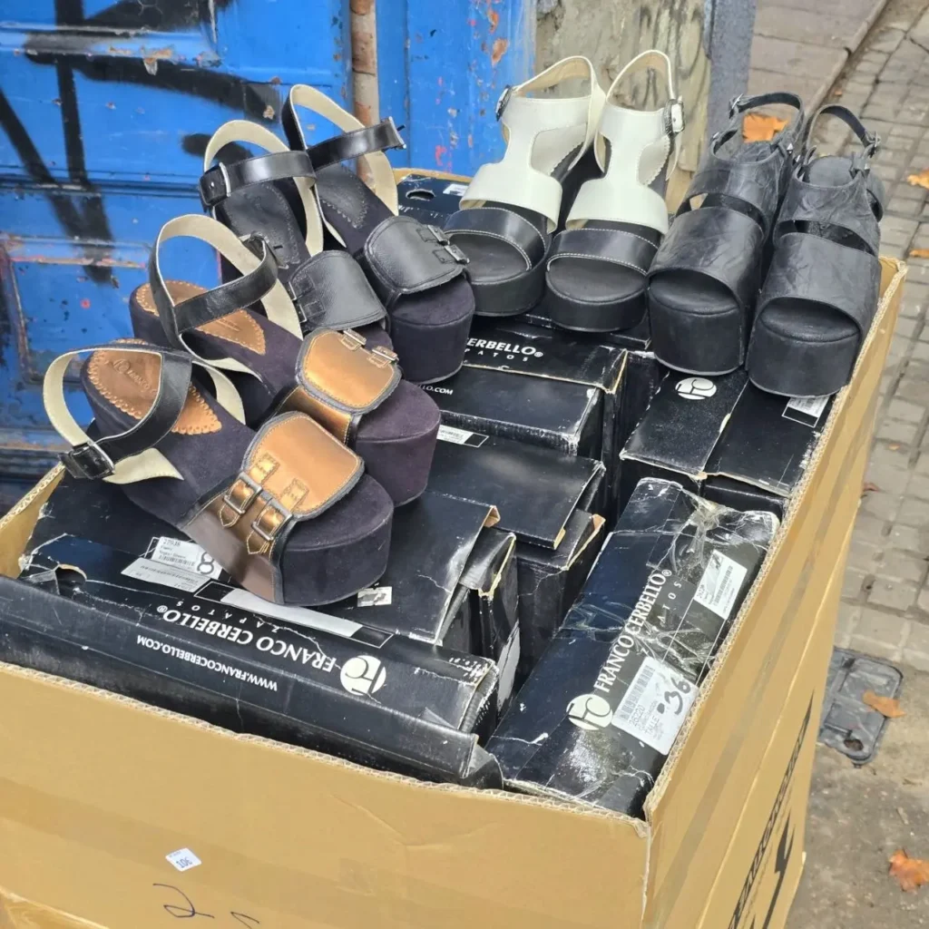 Varias sandalias de plataforma Franco Cerbello en colores negro, blanco y bronce, dentro de una caja de cartón sobre otras cajas de zapatos. by Remates Narvaja
