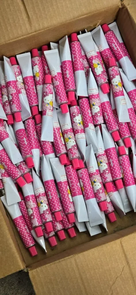 Caja de cartón llena de numerosos tubos rosas y blancos de Hello Kitty con lunares y tapas fucsia. by Remates Narvaja