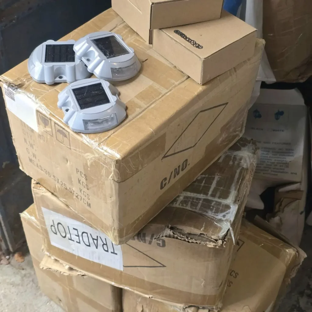 Tres marcadores solares de carretera grises con paneles solares sobre una pila de cajas de cartón de envío. by Remates Narvaja