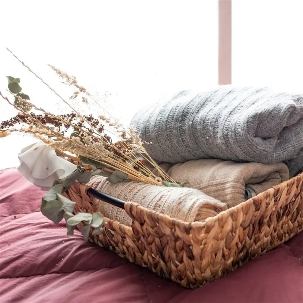 Cesta tejida con mantas y suéteres doblados, decorada con flores secas. by Remates Narvaja