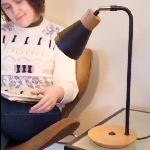 Lámpara de mesa moderna con pantalla negra y base de madera, iluminando a una persona leyendo un libro. by Remates Narvaja