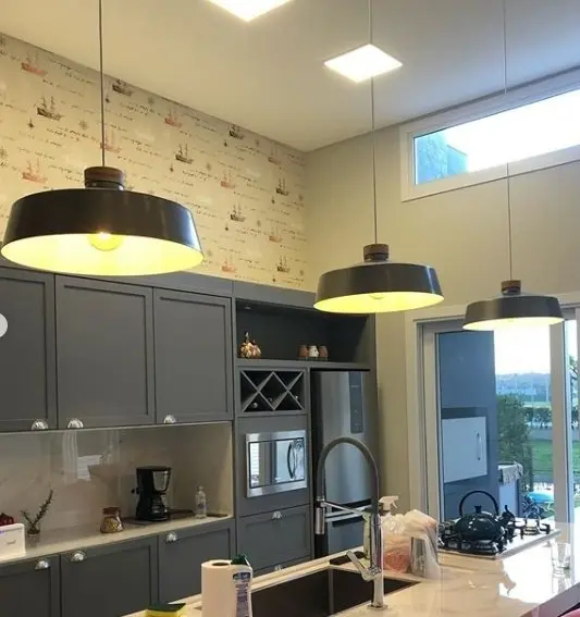 Cocina moderna con gabinetes grises, isla central, lámparas colgantes industriales y papel tapiz de barcos. by Remates Narvaja