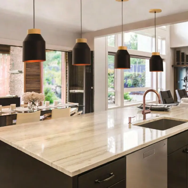 Cocina moderna con isla de encimera clara y cuatro lámparas colgantes negras con detalles dorados. by Remates Narvaja