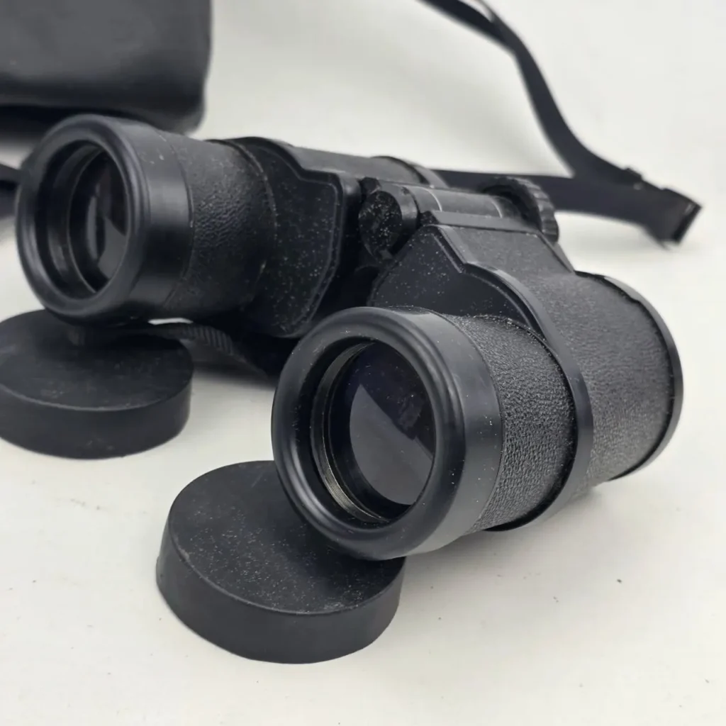 Binoculares negros con tapas de lente y correa sobre fondo blanco. by Remates Narvaja