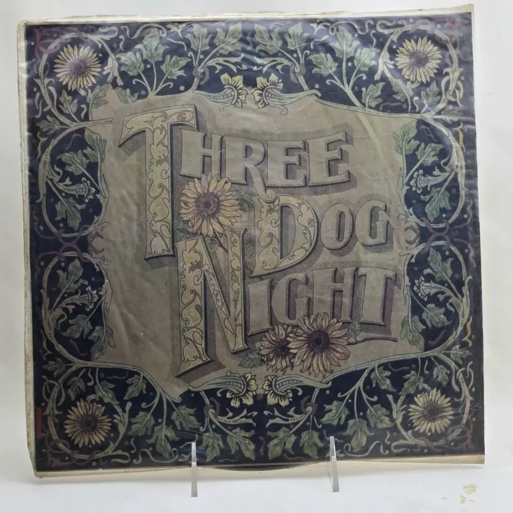 Portada de álbum de Three Dog Night con diseño floral ornamentado y girasoles. by Remates Narvaja