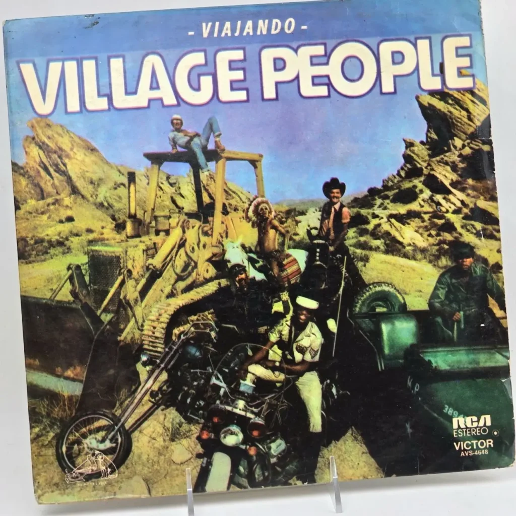 Portada del álbum "Viajando" de Village People con los miembros de la banda en sus trajes icónicos en un paisaje desértico by Remates Narvaja