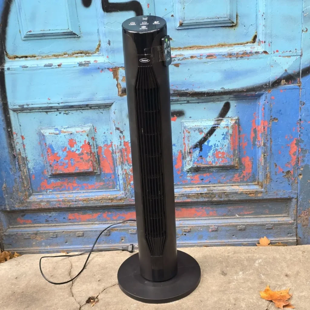 Ventilador de torre negro Kessel con control remoto frente a una puerta azul desgastada. by Remates Narvaja