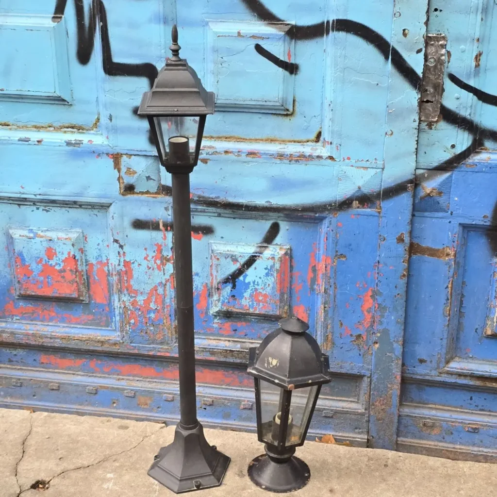 Dos faroles negros de metal frente a una puerta azul con pintura descascarada y graffiti. by Remates Narvaja