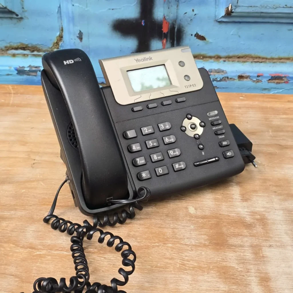 Teléfono IP Yealink T21P E2 negro con auricular y teclado sobre una superficie de madera. by Remates Narvaja