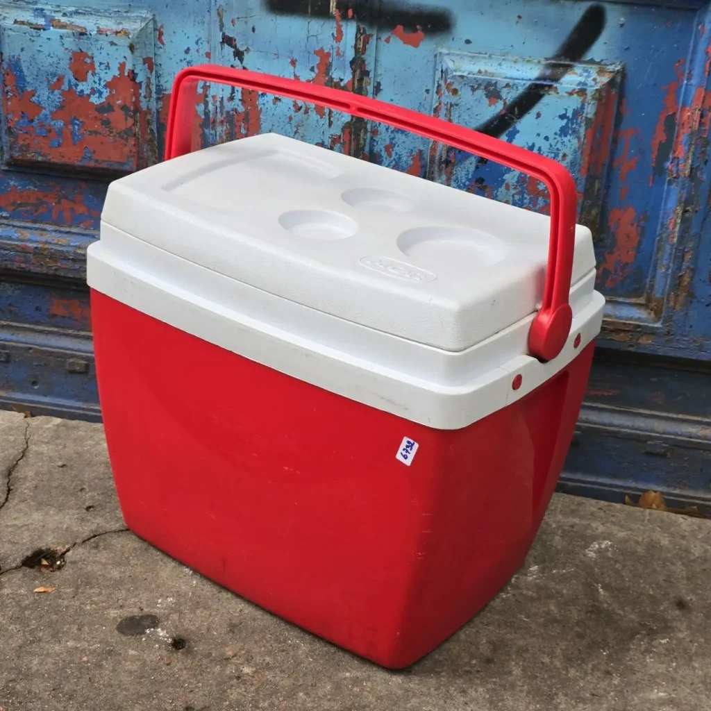 Nevera portátil roja y blanca con asa, sobre suelo de cemento. by Remates Narvaja