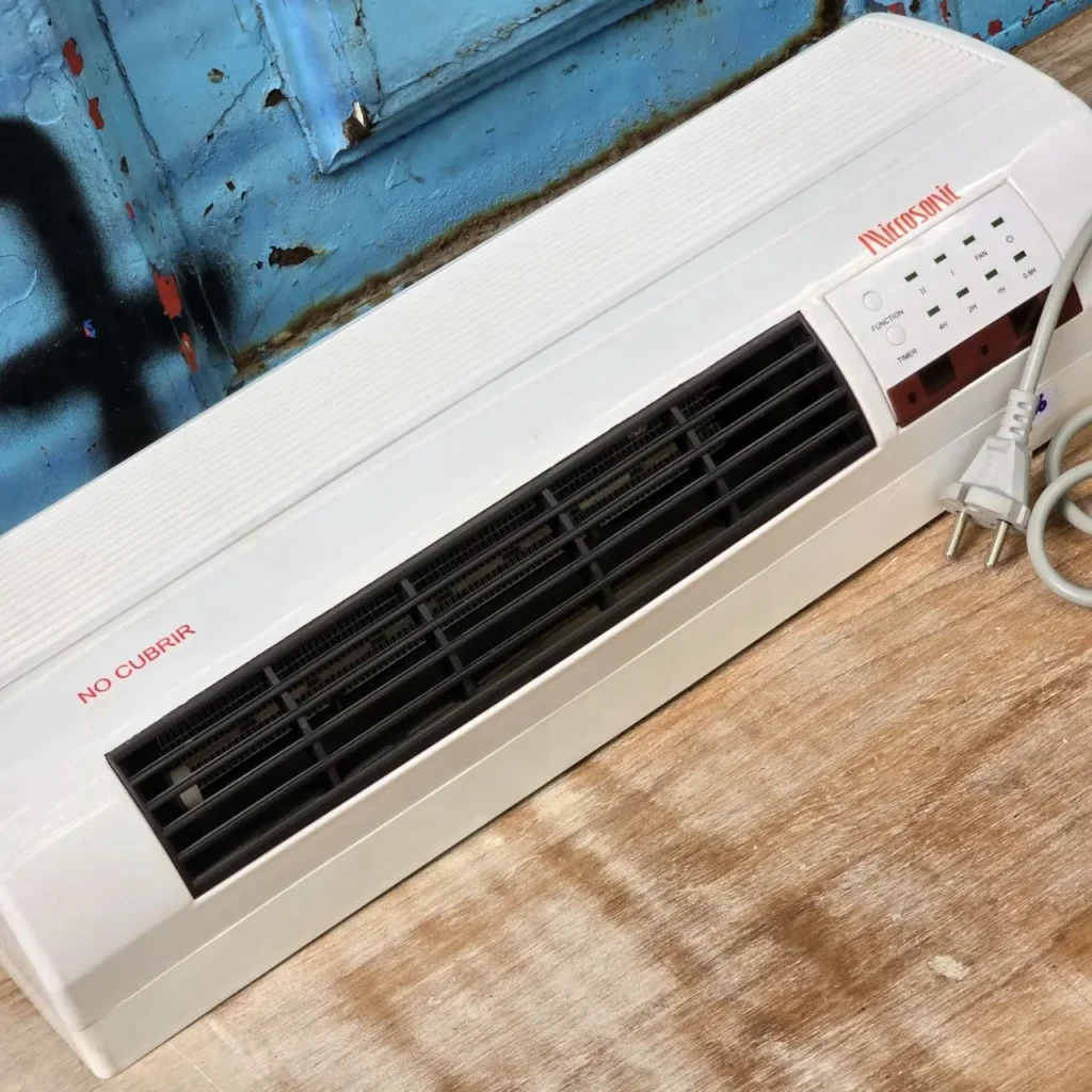 Calefactor eléctrico Microsonic blanco con panel de control y enchufe, sobre superficie de madera. by Remates Narvaja