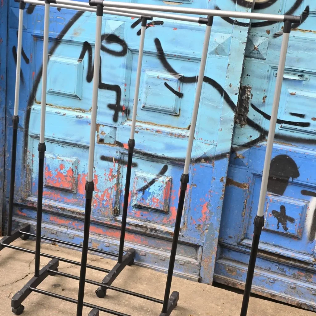 Perchero doble con ruedas frente a puerta azul desgastada con graffiti. by Remates Narvaja