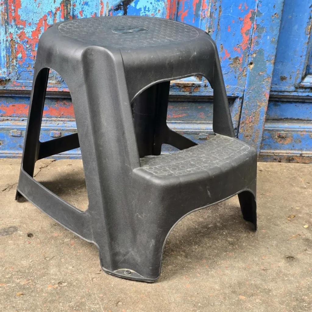 Taburete de dos escalones de plástico negro frente a una pared azul y roja desgastada. by Remates Narvaja