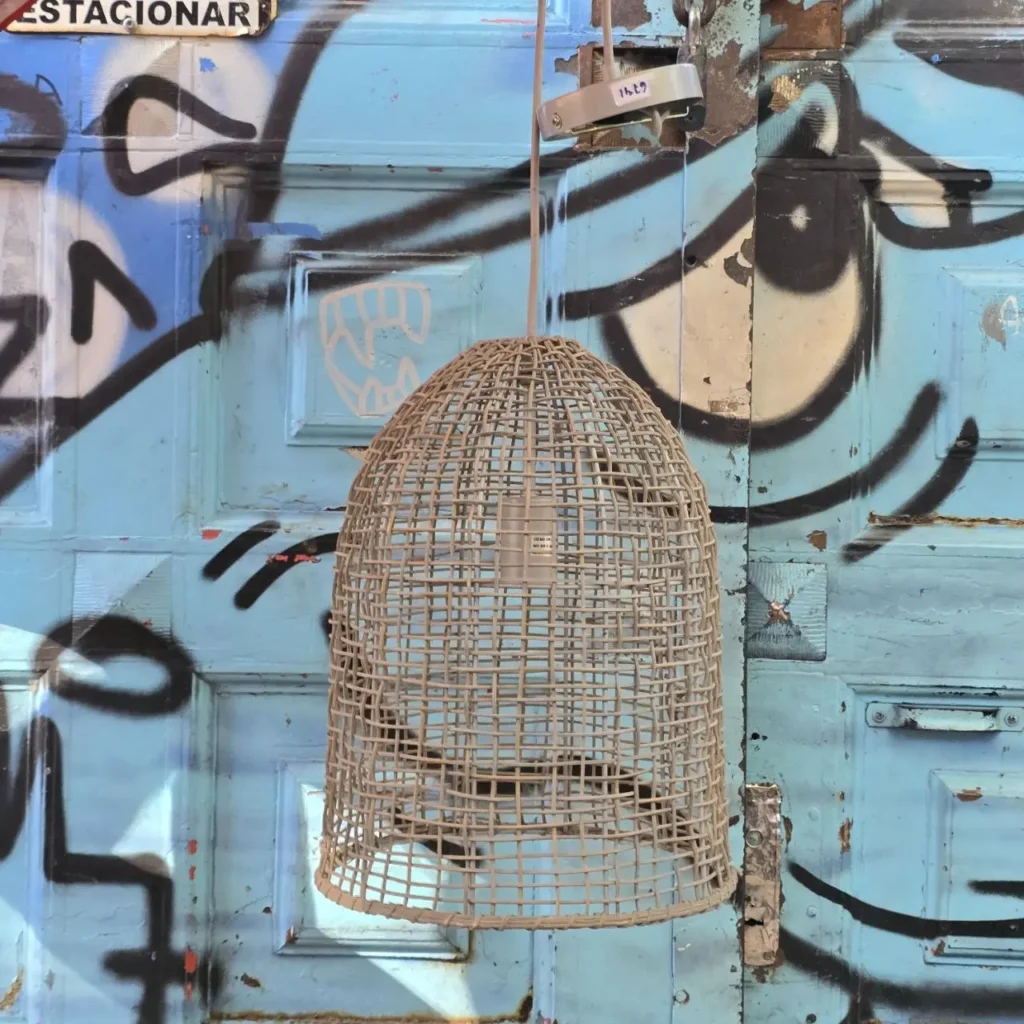 Lámpara colgante tejida frente a una puerta azul con graffiti urbano. by Remates Narvaja