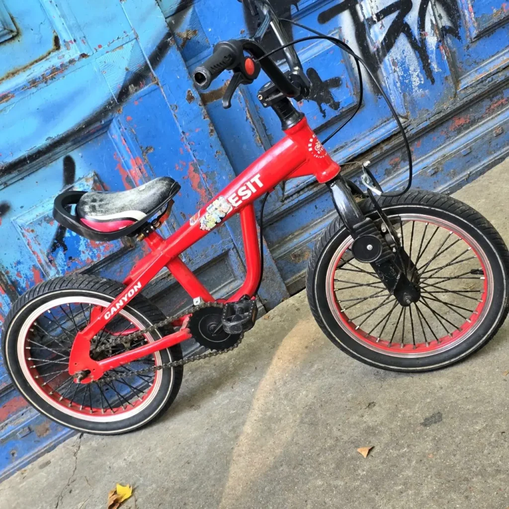 Bicicleta infantil roja ESIT con llantas rojas y detalles negros, apoyada contra una pared azul grafiteada. by Remates Narvaja