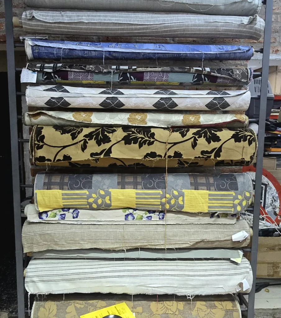 Rollos de tela con diversos estampados y texturas apilados en estanterías. by Remates Narvaja