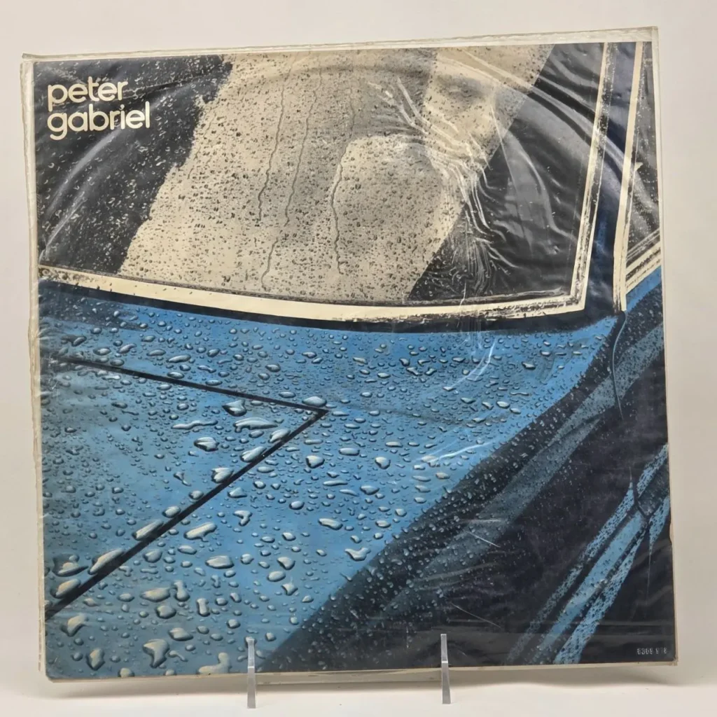 Portada del álbum de Peter Gabriel con un coche azul cubierto de gotas de lluvia. by Remates Narvaja