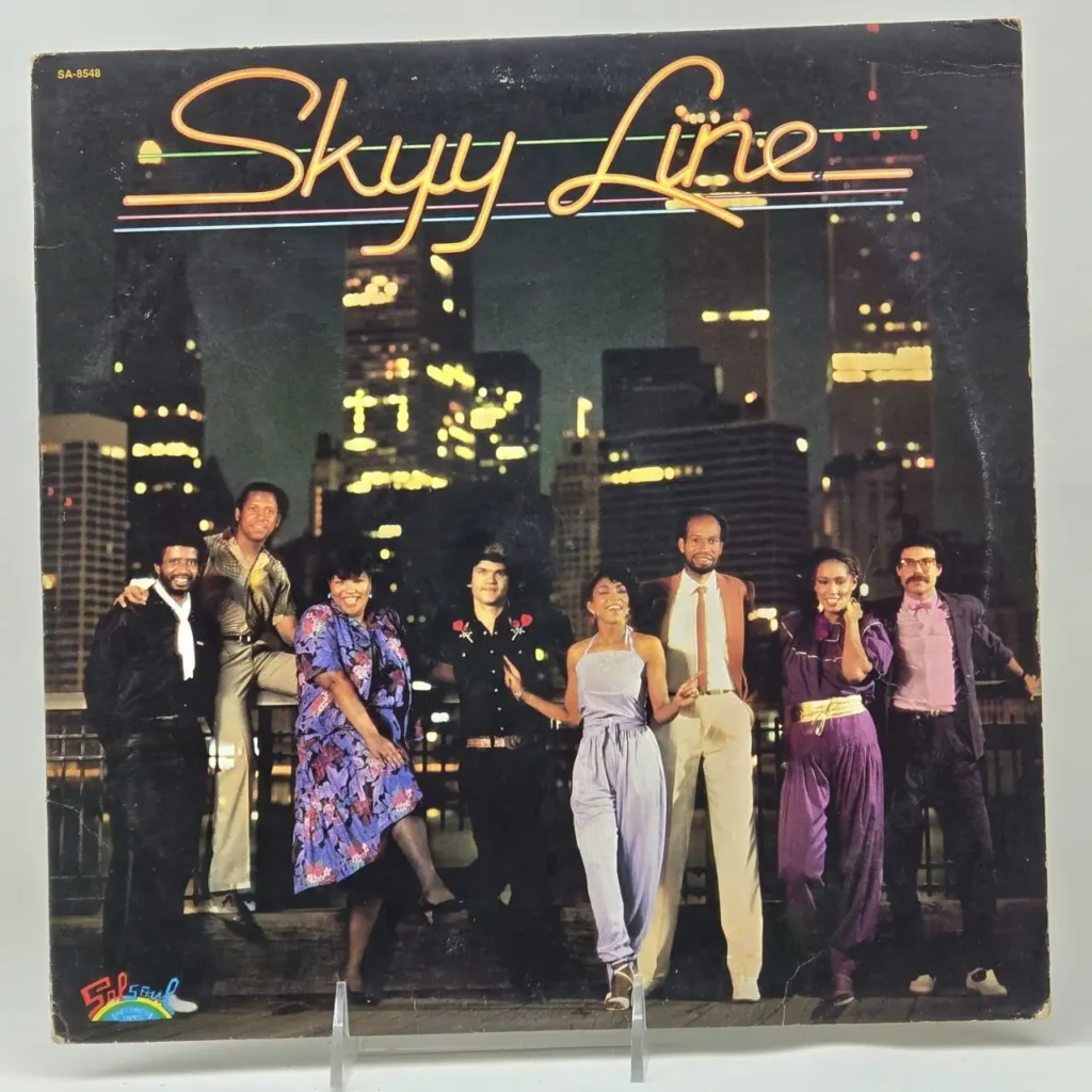 Portada del álbum "Skyy Line" con el grupo musical posando frente a un horizonte urbano nocturno. by Remates Narvaja
